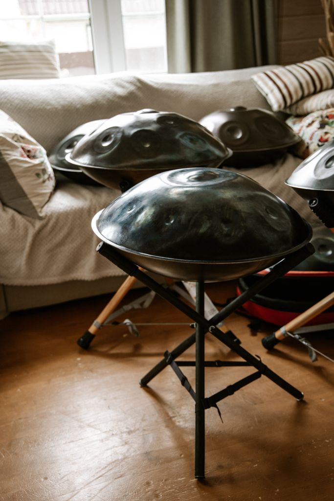 A set of handpans on stands in a cozy indoor setting with natural light streaming through a window.